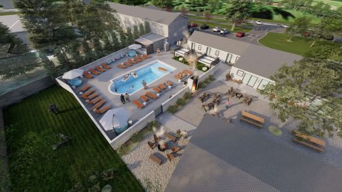 Aerial view of a hotel pool area with lounge chairs, a hot tub, and outdoor seating surrounded by greenery.