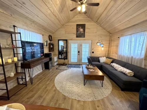 Cozy living room with wooden walls, a large sofa, TV, and a round rug, featuring natural light from large windows.