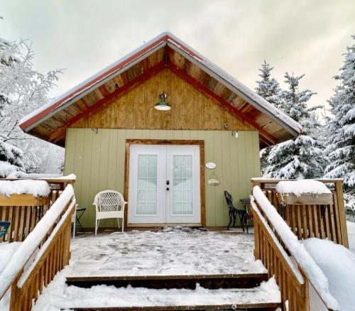 A cozy cabin with a wooden porch, surrounded by snow-covered trees under a cloudy sky.