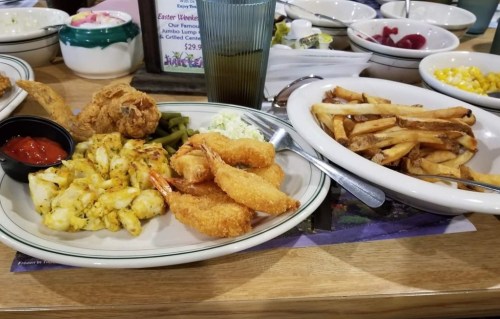 A plate of fried shrimp, seasoned shrimp, green beans, coleslaw, and fries with a side of dipping sauce.