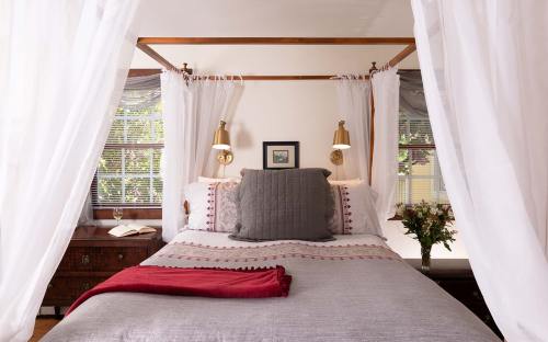 Cozy bedroom with a four-poster bed, soft linens, and natural light, featuring decorative pillows and a vase of flowers.