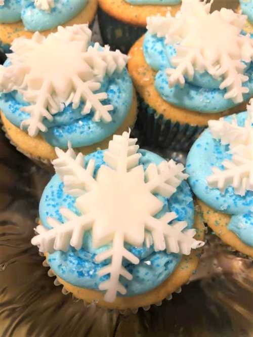 A close-up of cupcakes with blue frosting, topped with white snowflake decorations and blue sprinkles.