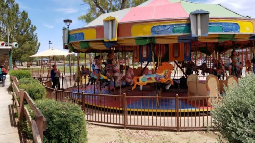 A colorful carousel with painted horses in a park, surrounded by greenery and people enjoying the day.