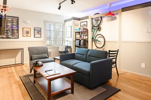 Cozy living room with a blue sofa, wooden coffee table, and bike decor on the wall, featuring hardwood floors and natural light.