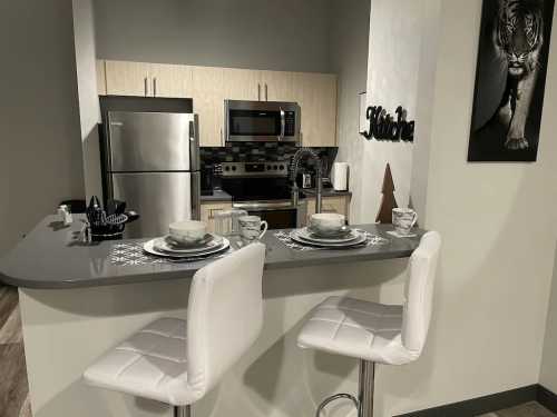 Modern kitchen with stainless steel appliances, a bar with two white stools, and a decorative tiger photo on the wall.