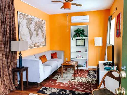 Cozy living room with orange walls, a map, a gray sofa, a wooden table, and decorative plants.