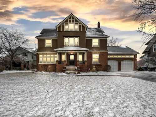 A large, two-story house with a snow-covered lawn, featuring a welcoming entrance and a sunset sky in the background.