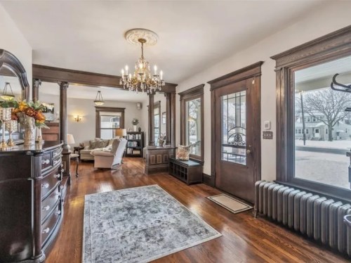 Bright living room with hardwood floors, elegant chandelier, and large windows, featuring a cozy seating area and decorative accents.