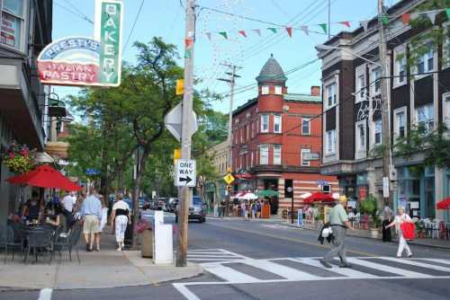 A lively street scene with a bakery, outdoor seating, and colorful buildings under a clear blue sky.