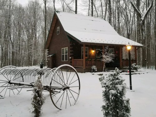 A cozy wooden cabin in a snowy forest, with a vintage cart and a lamp post in the foreground.