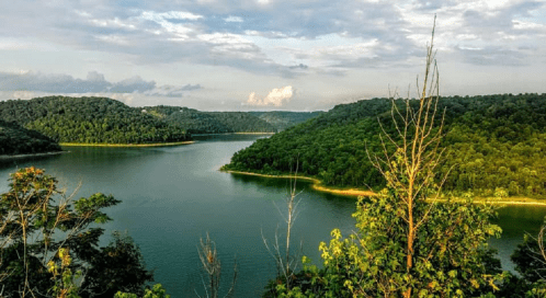 A serene lake surrounded by lush green hills under a partly cloudy sky.