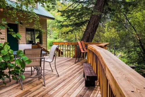 A wooden deck surrounded by trees, featuring chairs and a table, creating a cozy outdoor space.