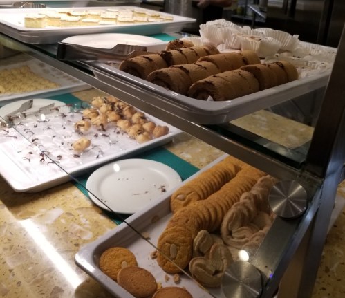 A display of assorted baked goods, including cookies and pastries, arranged on trays in a dessert showcase.