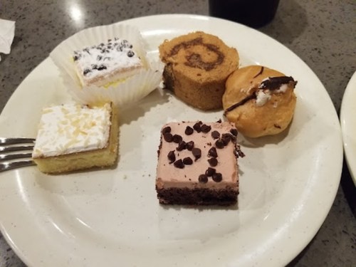 A plate with assorted desserts: a chocolate brownie, a cream-filled pastry, a roll cake, and two small squares of cake.