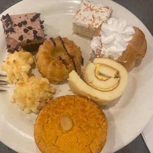 A plate with various desserts: chocolate cake, coconut macaroons, mini bundt cakes, a rolled cake, and a cookie.