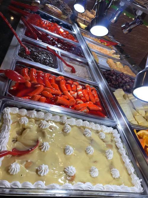 A dessert buffet featuring various colorful jellies, cakes, and fruits under bright lights.
