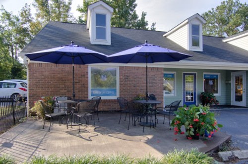Outdoor seating area with blue umbrellas, tables, and chairs in front of a cozy bakery and coffee shop.