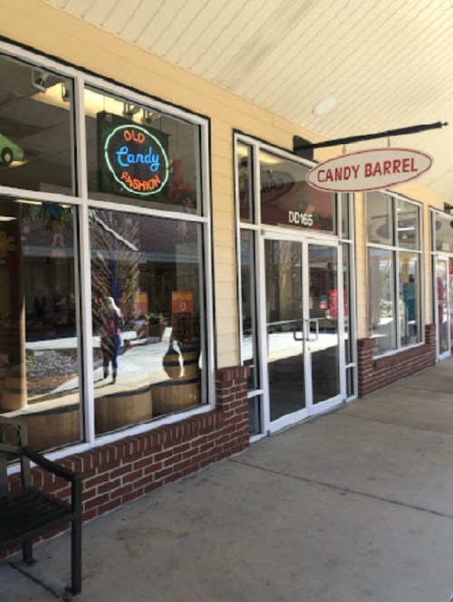 Exterior of a candy store called "Candy Barrel," featuring large windows and a colorful neon sign.