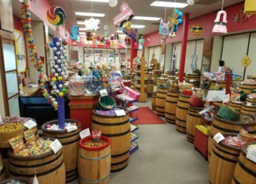 Colorful candy store filled with barrels of sweets, decorations, and vibrant displays throughout the cheerful interior.