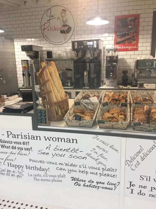 A bakery display with baguettes and pastries, featuring a sign that says "La Parisienne" and various French phrases.