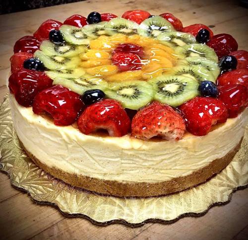 A colorful fruit-topped cheesecake with strawberries, kiwi, blueberries, and a glossy glaze on a decorative base.