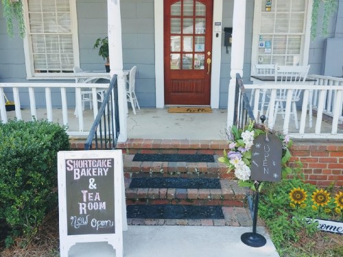 A charming entrance to Shortcake Bakery & Tea Room, featuring a welcoming sign and flower arrangements.