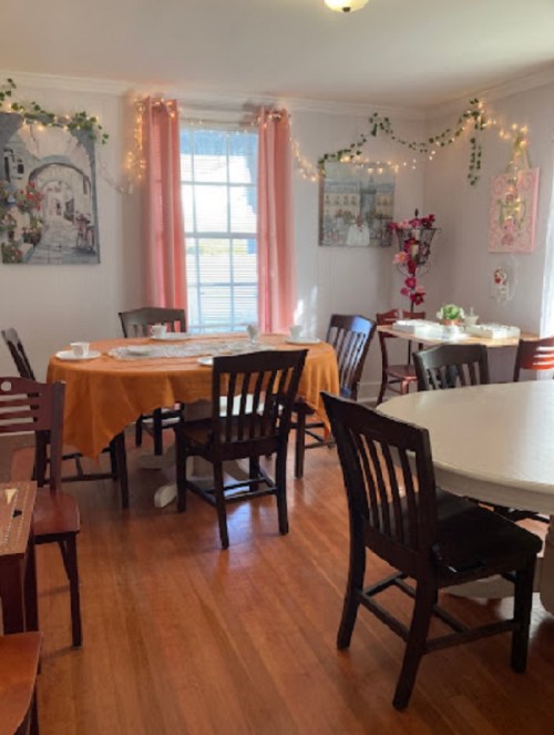 Cozy dining area with wooden tables, chairs, and soft lighting, decorated with plants and artwork.