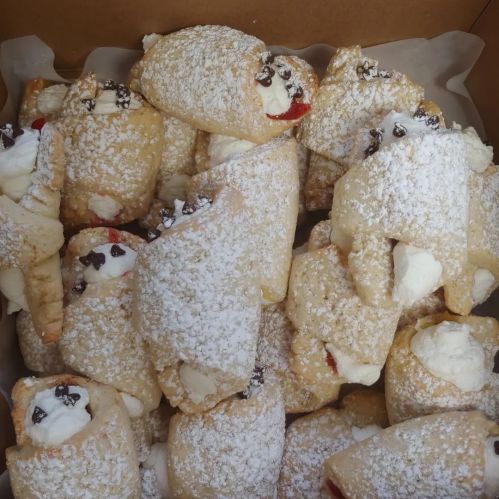 A box filled with cream-filled pastries dusted with powdered sugar and decorated with chocolate chips and cherries.