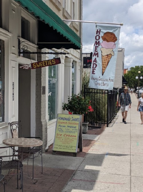 A storefront with a sign for "Homemade Sweets" and an ice cream banner, featuring a cone and outdoor seating.