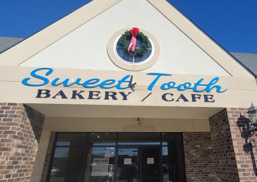 Sign for "Sweet Tooth Bakery / Cafe" with a festive wreath, set against a clear blue sky.