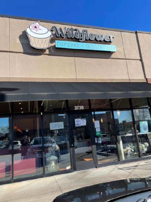 Exterior of Wildflower Cupcake + Dessert Bar, featuring a sign and open door, with a clear blue sky above.