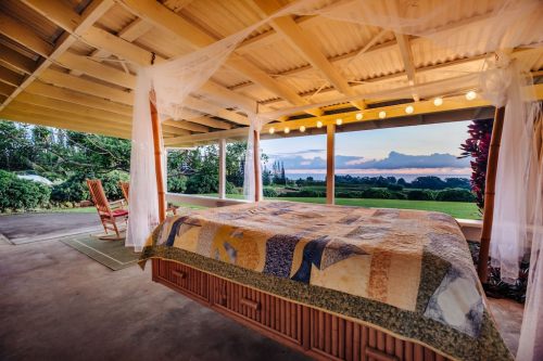 Cozy bedroom with a quilted bed, rocking chair, and large windows showcasing a scenic sunset view.