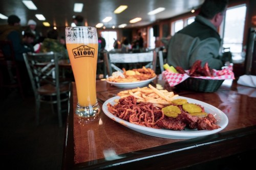A plate of fried chicken with pickles and fries, alongside a glass of beer, in a cozy restaurant setting.