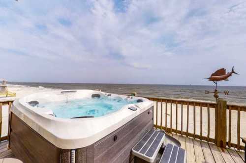 A hot tub on a deck overlooking a beach and ocean under a cloudy sky.
