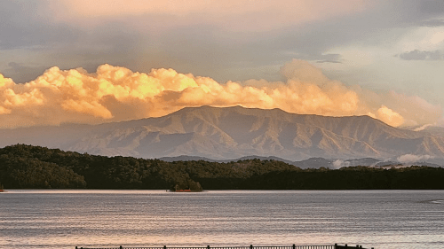 A serene landscape featuring mountains in the background, with golden clouds above and a calm body of water in the foreground.