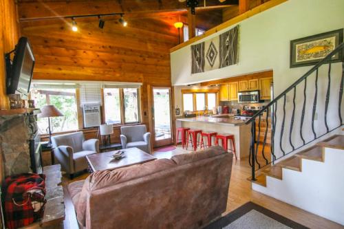 Cozy cabin interior featuring a living area, kitchen, and staircase with wooden accents and large windows.