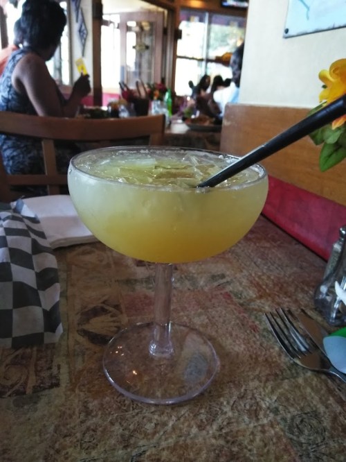 A large margarita in a glass with a straw, sitting on a table in a restaurant with people in the background.