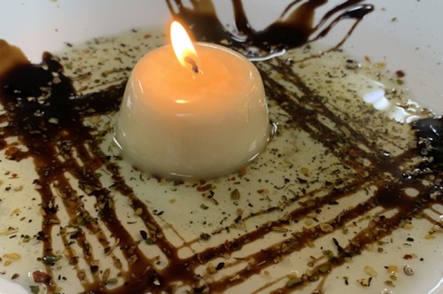 A lit candle sits in a shallow dish filled with oil and spices, creating a warm, inviting ambiance.
