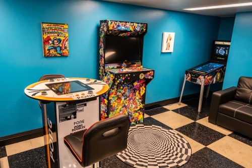 A vibrant game room featuring arcade machines, a colorful wall, and a black and white spiral rug.
