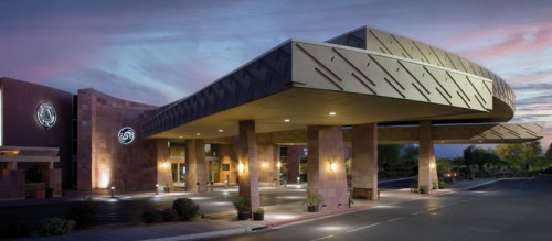 Modern hotel entrance with a distinctive architectural design, illuminated at dusk under a colorful sky.