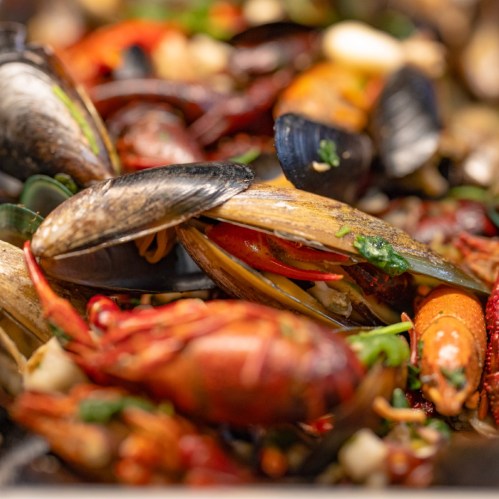 A close-up of a colorful seafood dish featuring mussels, shrimp, and spices, garnished with herbs.