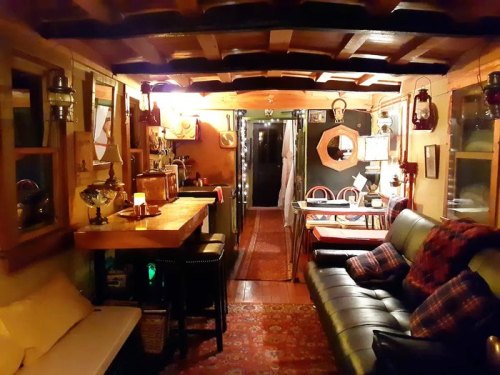 Cozy interior of a rustic cabin with wooden beams, a sofa, dining area, and warm lighting.