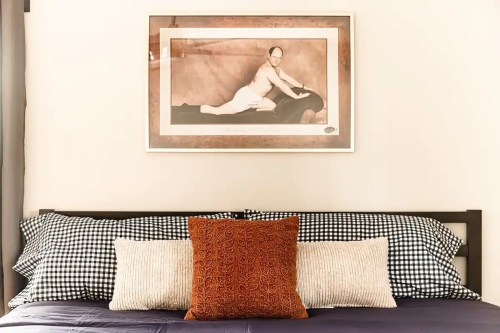 A bed with patterned pillows and a framed vintage photo of a person lying on a surface above it.