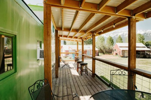 A wooden deck with chairs overlooks a green building and scenic mountains in the background.