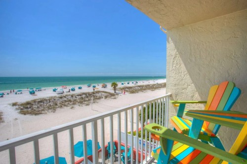 Colorful chairs on a balcony overlooking a sandy beach and turquoise ocean under a clear blue sky.