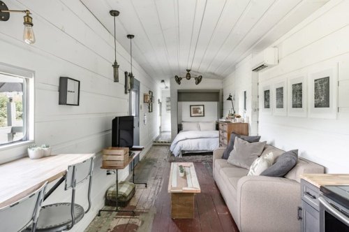 Cozy interior of a tiny home featuring a living area, dining table, and a bedroom with a bed and wooden accents.