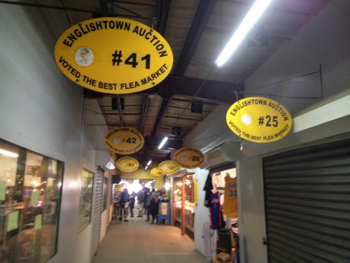 Interior of a flea market with yellow signs displaying auction numbers and "Voted the Best Flea Market" banners.