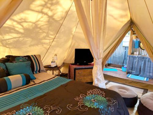 Cozy glamping tent interior with a bed, TV, and seating area, featuring warm lighting and decorative pillows.