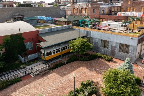 Aerial view of a brick courtyard with a yellow train car, surrounded by greenery and buildings in an urban setting.