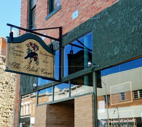 Sign for "The Black Crow" restaurant, featuring a horse silhouette, on a brick building with large windows.